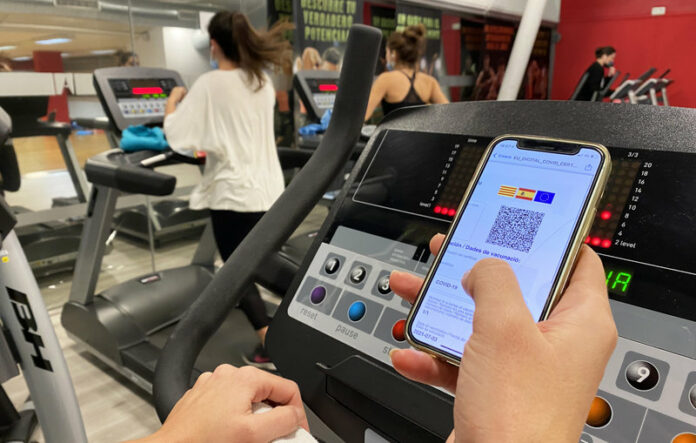 Gimnàs amb gent amb mascareta, mirant el passaport COVID